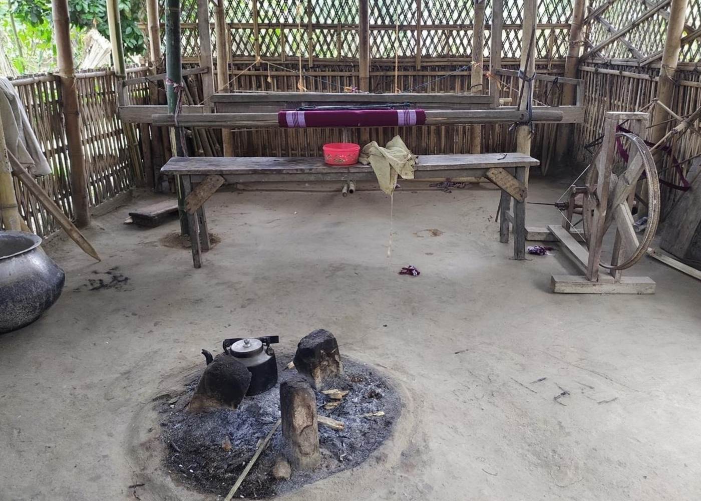 Kitchen and livelihood, a dual responsibility shouldered by women, with a traditional cookstove in the background and a handloom representing the balance between household care and income generation